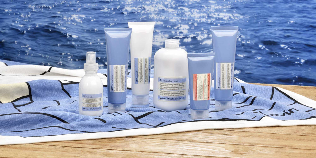 Davines SU Hair Care Line displayed on a towel by the ocean, including Hair Milk, Hair & Body Wash, Hair Mask, and Aftersun products.