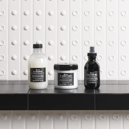 Three Davines oi hair care products on a black surface with a white tiled wall background bombshell salon delmar ny