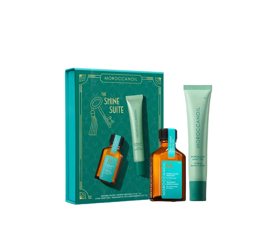 Moroccanoil 'The Shine Suite' haircare gift set featuring a teal gift box, a small amber bottle, and two teal tubes, arranged on a light marble surface against a warm off-white background.
