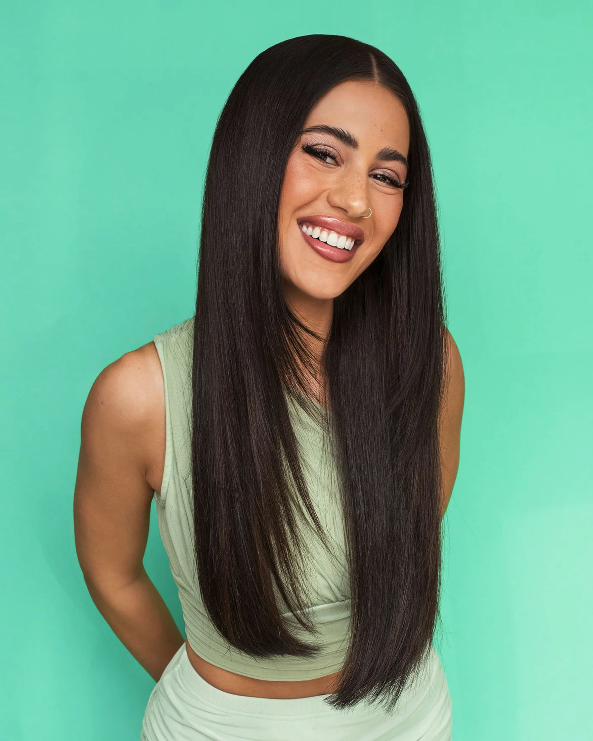 Woman with long straight hair smiling against a teal background