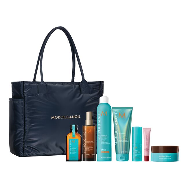 Moroccanoil gift set featuring a navy blue nylon tote bag with gold lettering, accompanied by various hair care products in turquoise, orange, brown, and pink on a solid white background.
